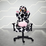 Front view of the techni sport cow gaming chair in black and white in a white room with grey floor. This cow print gaming chair features a black base. The cow chair headrest pillow has light brown horns and ears lined with fluffy pink material and the lumbar pillow has matching fluffy pink to compliment the design. This is definitely one of the cutest Techni Sport Gaming chair options and a great option for cute gaming setups or home office setups.