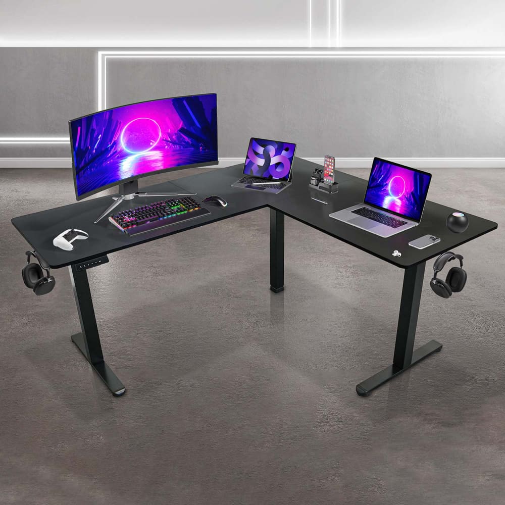 Black L-shape electric sit-to-stand desk with monitor, laptop, and accessories on it in a room