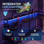 A gaming desk setup with integrated RGB LED lighting under the desk, on the monitor stand, and around the peripherals, shown in a dark room with a brick wall. A large text overlay at the top reads 'INTEGRATED LED LIGHTING' and a feature summary panel at the bottom lists color options and modes. 