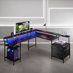 An L-shaped gaming desk with a black frame and a glowing blue LED under-glass desktop surface, styled with a computer tower, monitor, keyboard, lamp, and accessories in a modern room setting. 