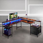An L-shaped gaming desk with a dark wood grain top and black metal frame, styled with a computer tower, monitor, keyboard, lamp, and accessories. The desk is set in a modern room with gray walls and concrete floors. 