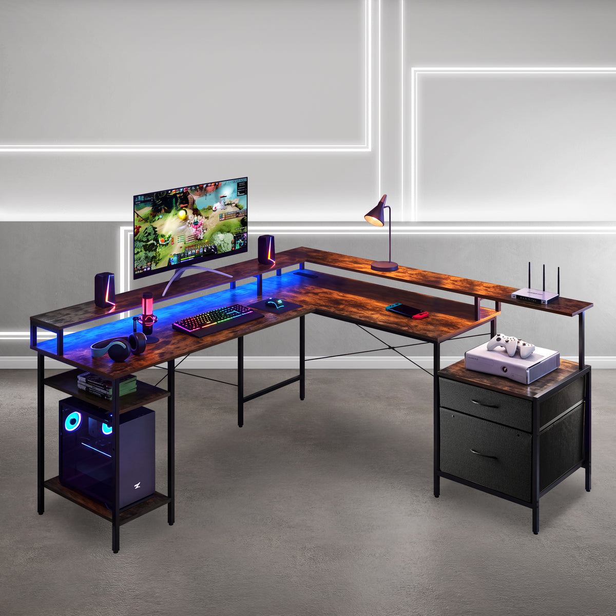 An L-shaped gaming desk with a dark wood grain top and black metal frame, styled with a computer tower, monitor, keyboard, lamp, and accessories. The desk is set in a modern room with gray walls and concrete floors. 